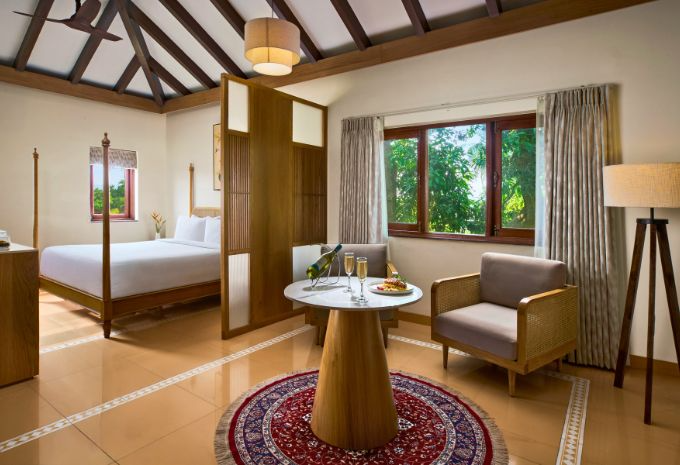 Four-poster king bed under vaulted thatched ceiling with garden views at Mercure Goa Devaaya Boutique Villa