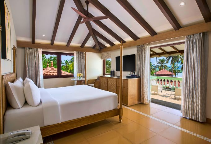 Four-poster bedroom with vaulted beam ceiling and private terrace overlooking palm trees at Mercure Goa Devaaya Resort Divar Island